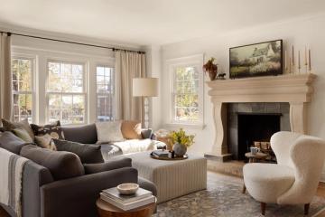 Neutral transitional living room with charcoal sectional, cream accent chair, and light wood fireplace mantel creating a balanced, sophisticated atmosphere