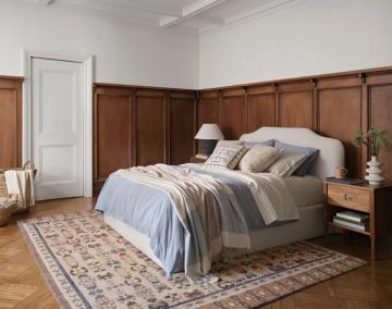 Classic bedroom with rich wood paneling headboard, layered neutral textiles, and vintage area rug
