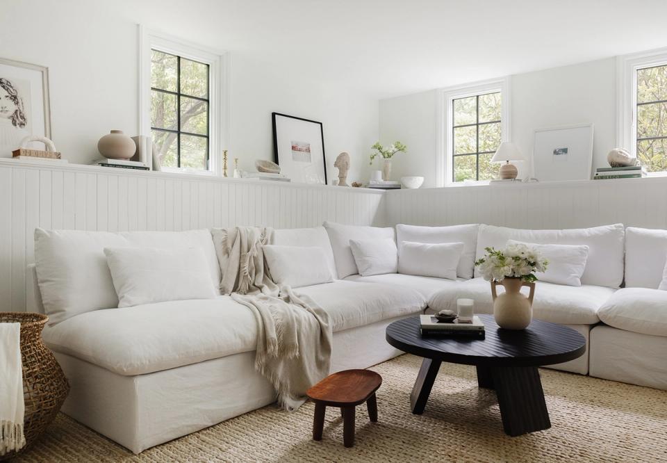 Warm minimalist living room with cream sectional, black round table, and natural wood accents