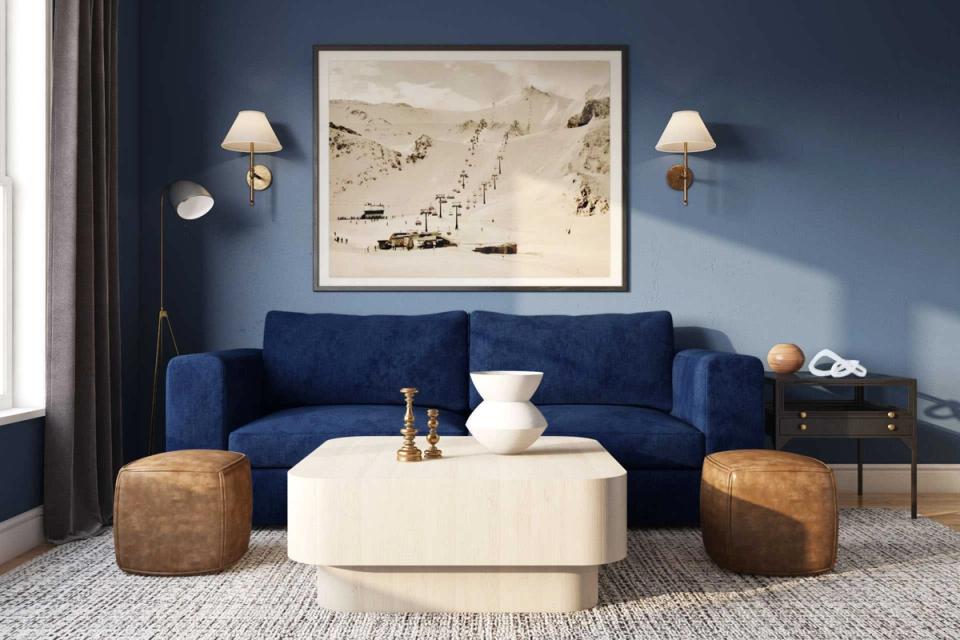 Contemporary living room with deep blue walls, navy sofa, cream ottoman, and warm wood accents