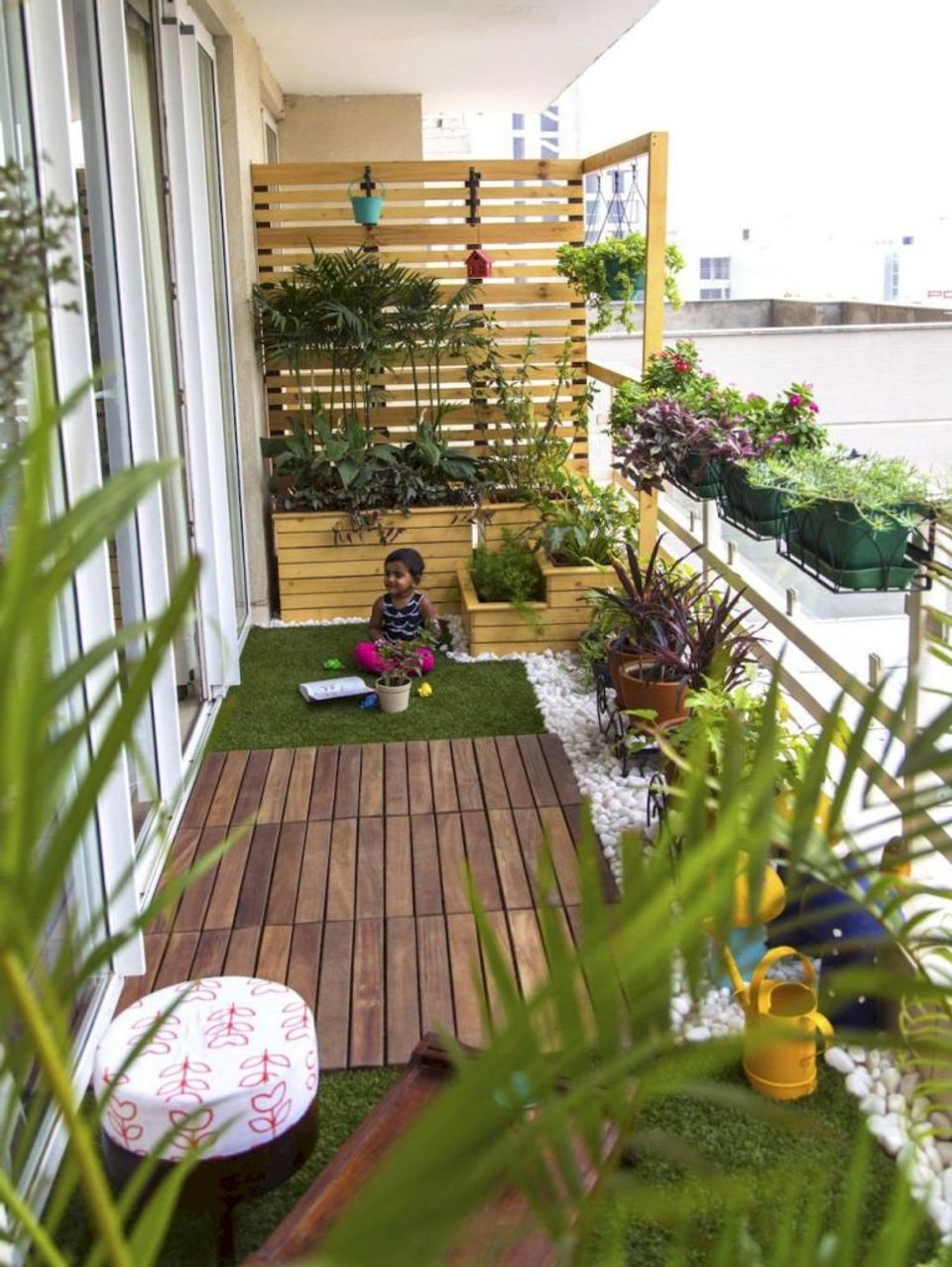 Lush garden balcony with wooden slatted privacy screen, vibrant potted plants, artificial turf, and playful seating creating a green urban oasis.