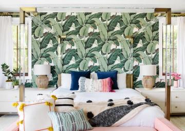 Tropical bedroom with bold botanical wallpaper, gold canopy frame, and colorful accent pillows against white bedding