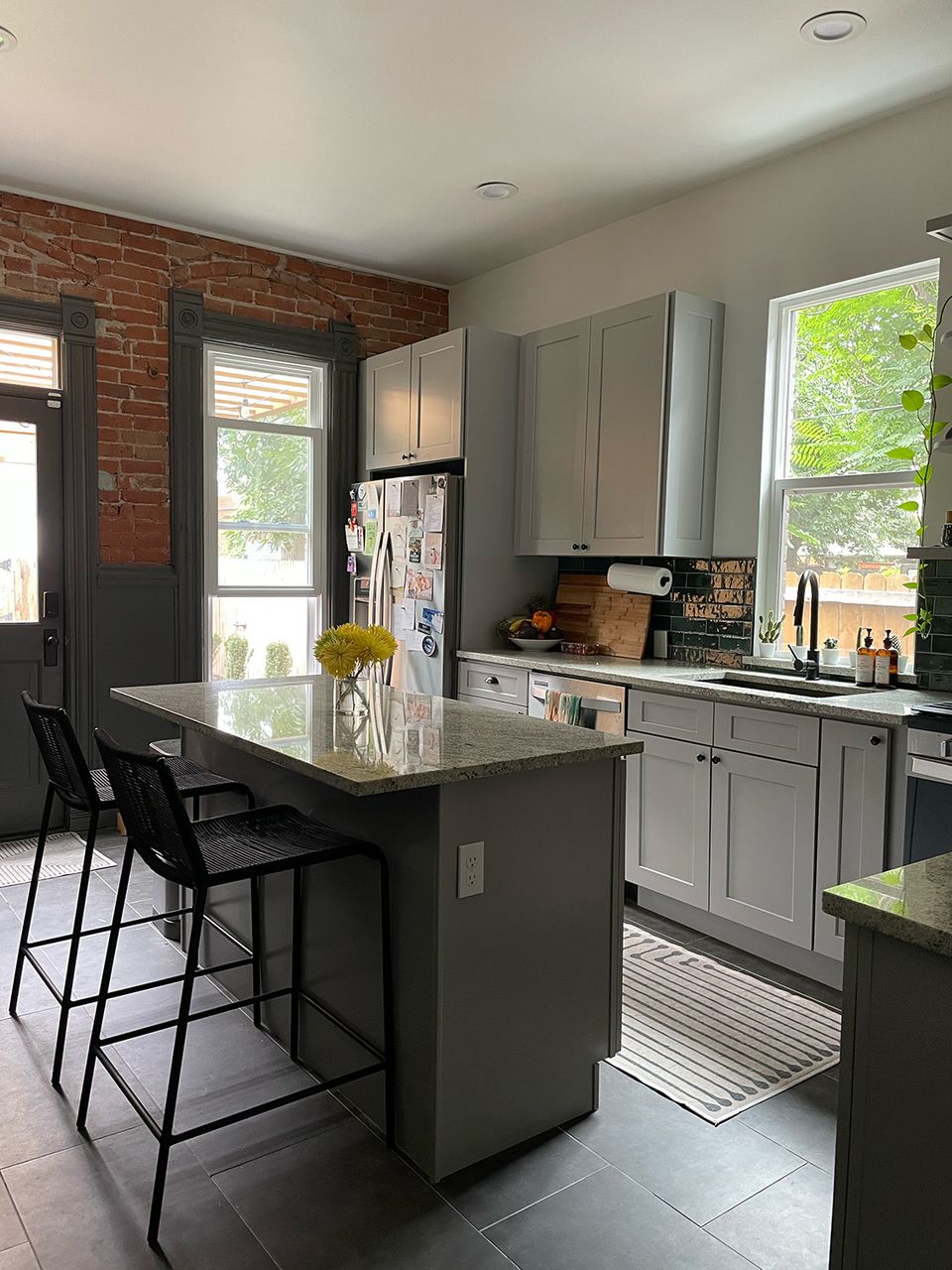 Transitional kitchen blending sage green painted cabinets with exposed brick and industrial black island