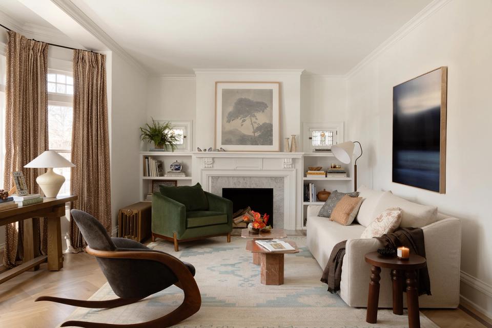 Modern maximalist living room with forest green sofa, warm wood accents, fireplace, and curated art collection