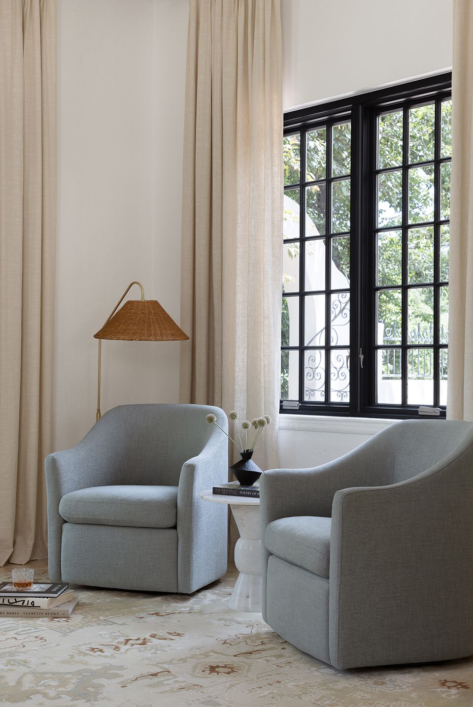 Modern minimalist seating area with gray upholstered chairs, floor lamp, black-framed windows, and flowing neutral drapery