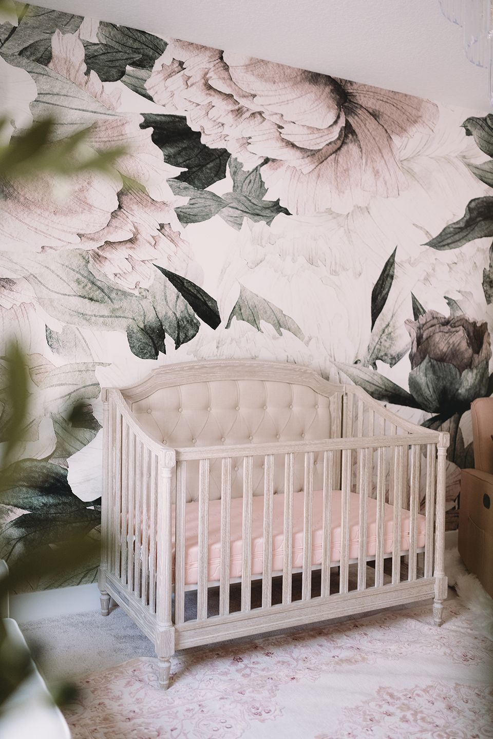 Delicate botanical wallpaper with pink peonies and green foliage behind white crib