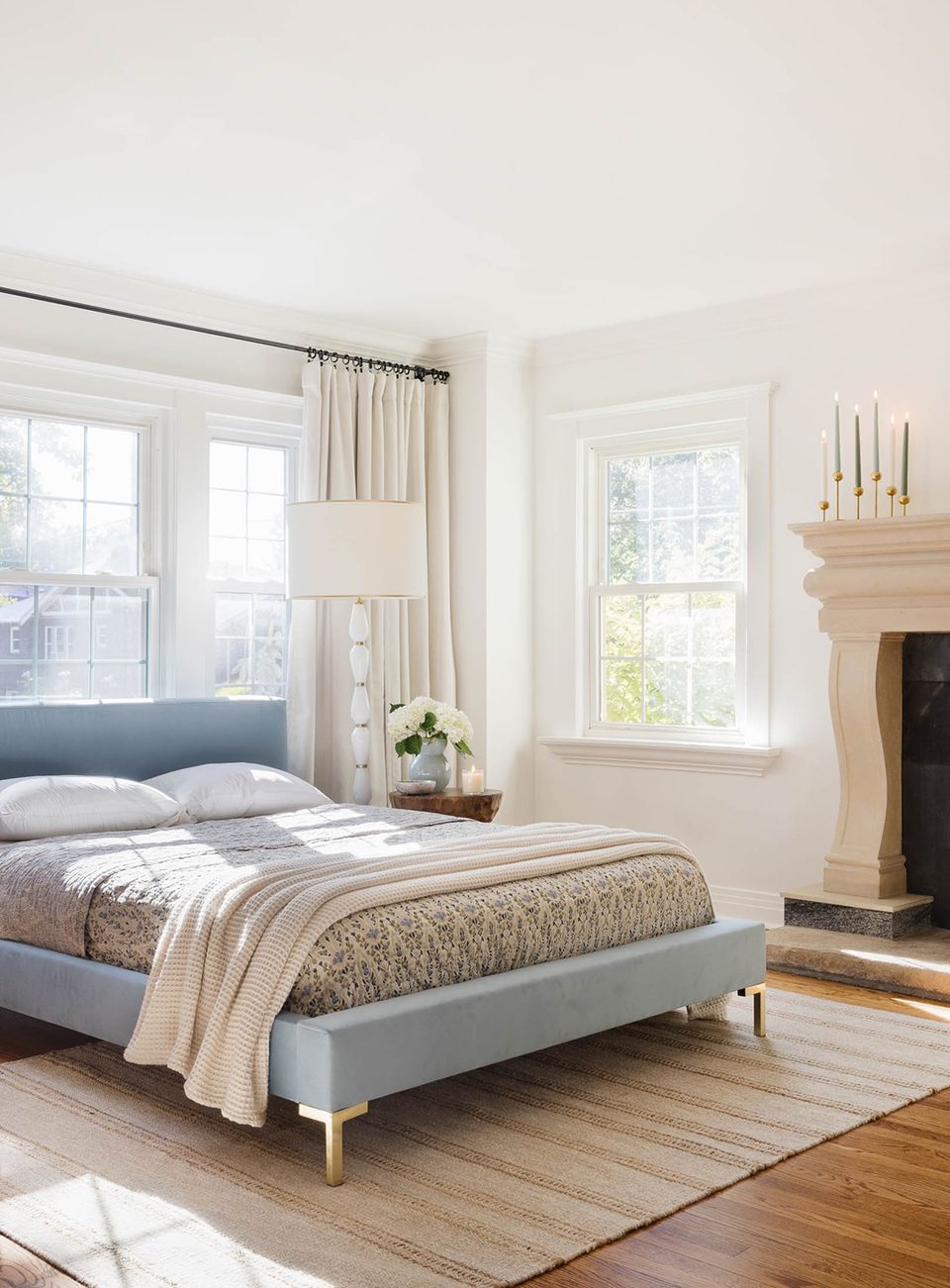 Serene minimalist bedroom with soft blue upholstered bed, neutral textiles, fireplace, and abundant natural light
