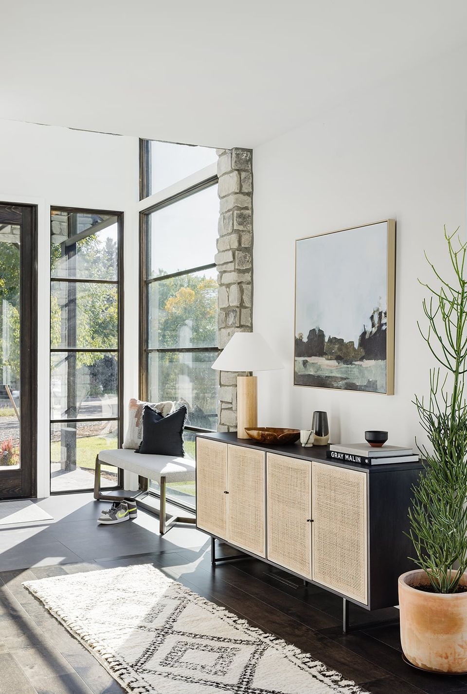 Mid-century modern entryway with natural light, caned cabinet, and contemporary landscape art