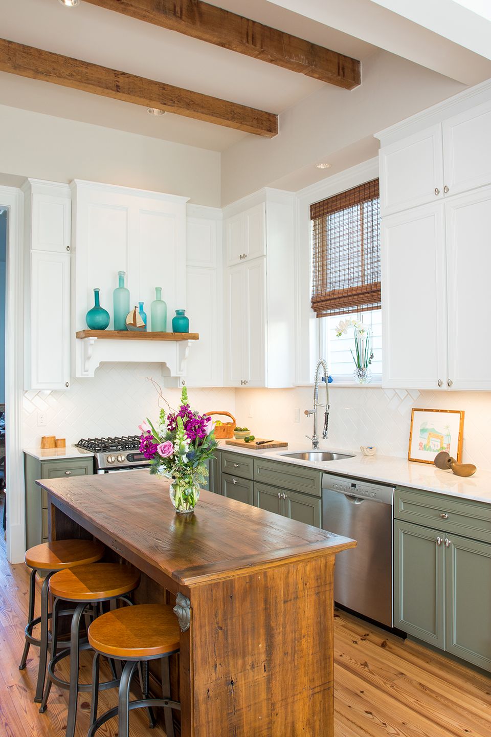 Farmhouse kitchen blending sage green cabinetry, white shelving, exposed beams, and warm wood island