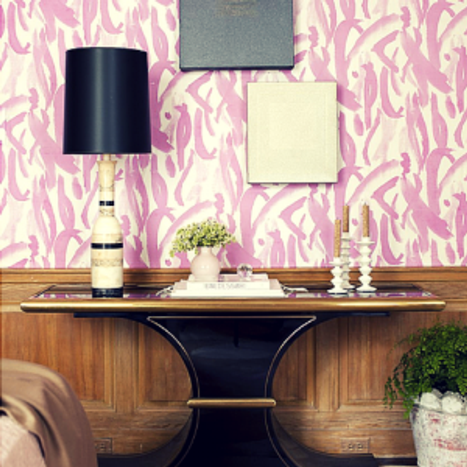 Eclectic console styling: pink patterned wallpaper, wood base, black lamp, and classic accessories