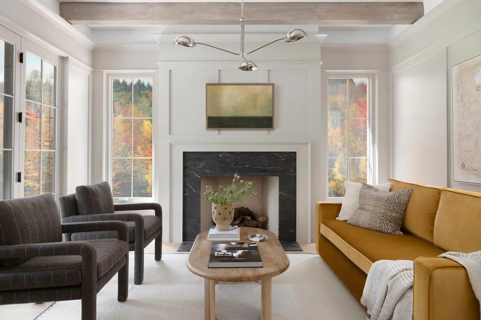 Contemporary living room with fireplace, mustard sofa, gray seating, wood oval table, and bright windows