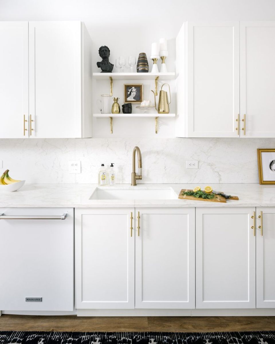 Contemporary kitchen with white cabinetry, brass hardware, floating shelves, and clean aesthetic