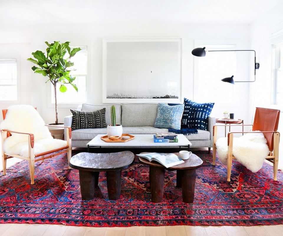 Eclectic living room with vibrant red rug, mid-century chairs, and bold patterned pillows creating dynamic warmth