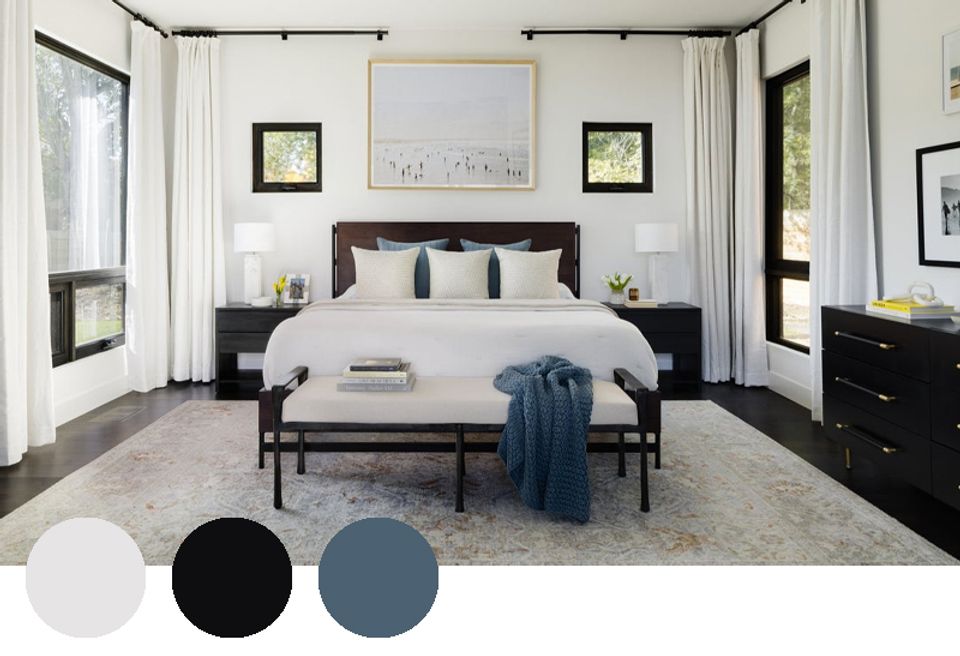 Modern master bedroom with black bed frame, crisp white linens, slate blue accents, and abundant natural light creating serene elegance.