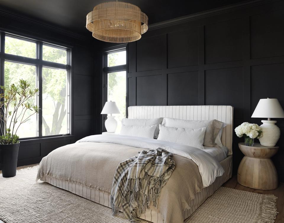 Dramatic dark moody bedroom with black paneled walls, white upholstered bed, and warm brass accents creating sophisticated contrast