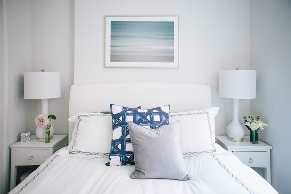 Serene coastal bedroom with white bedding, navy accents, and soft blue landscape artwork