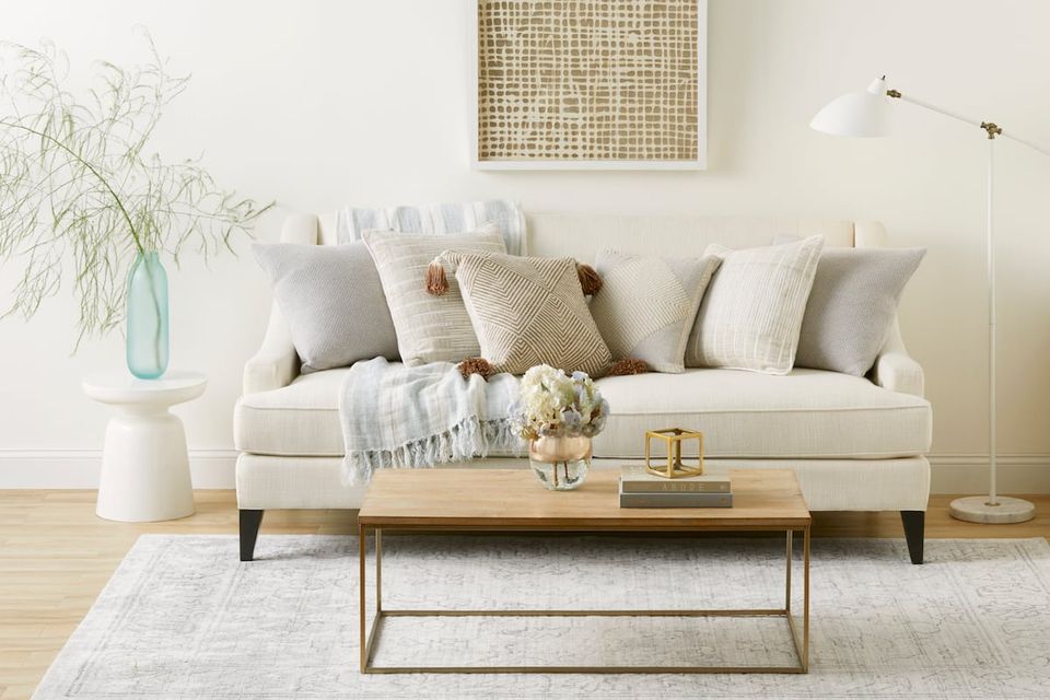 Minimalist spring living room with cream sofa, layered neutral pillows, and natural wood accents creating an airy, serene atmosphere.