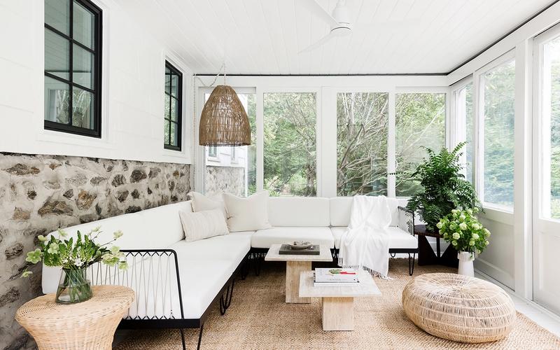 Bright sunroom with coastal minimalist design, cream seating, natural textures, and abundant greenery