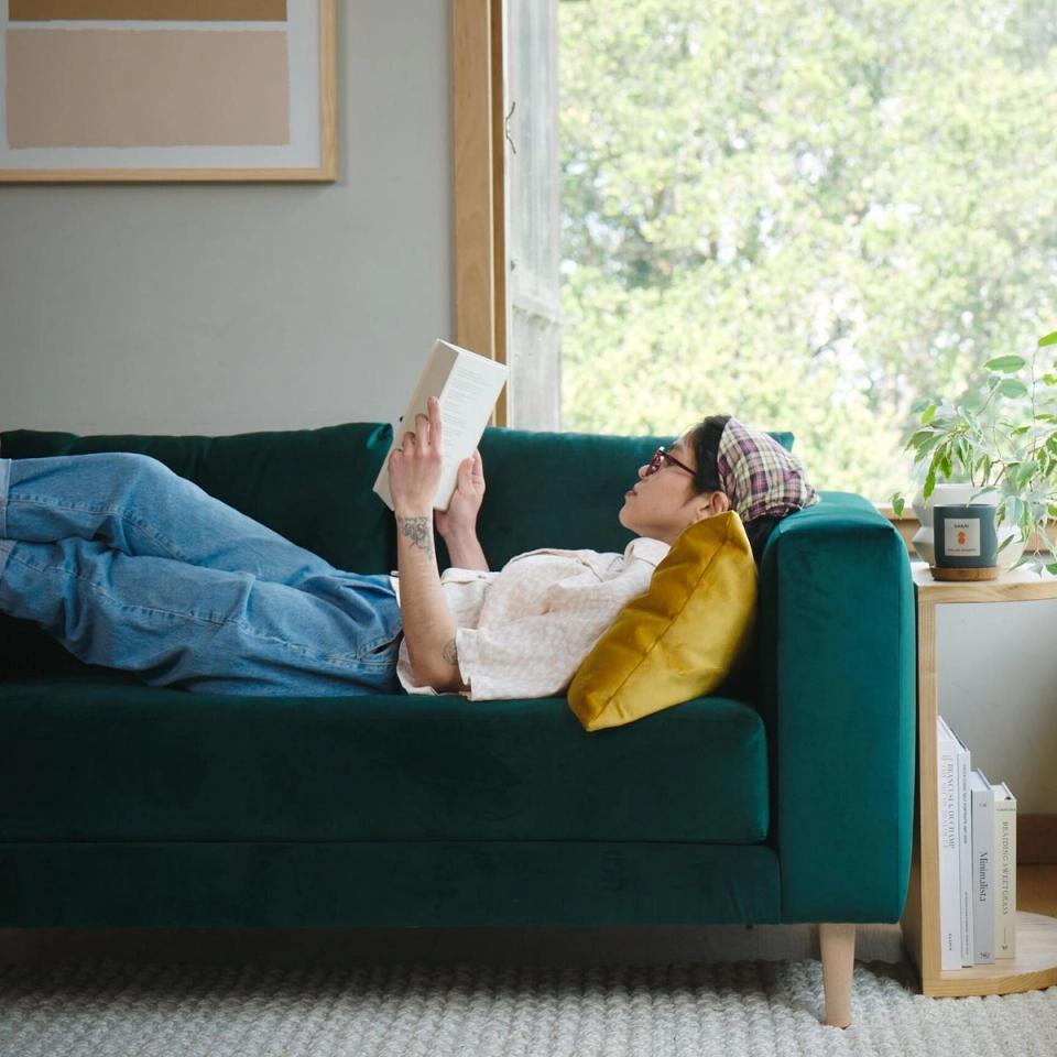 Cozy modern interior with emerald sofa, mustard yellow accent pillow, bright natural light, warm wood tones
