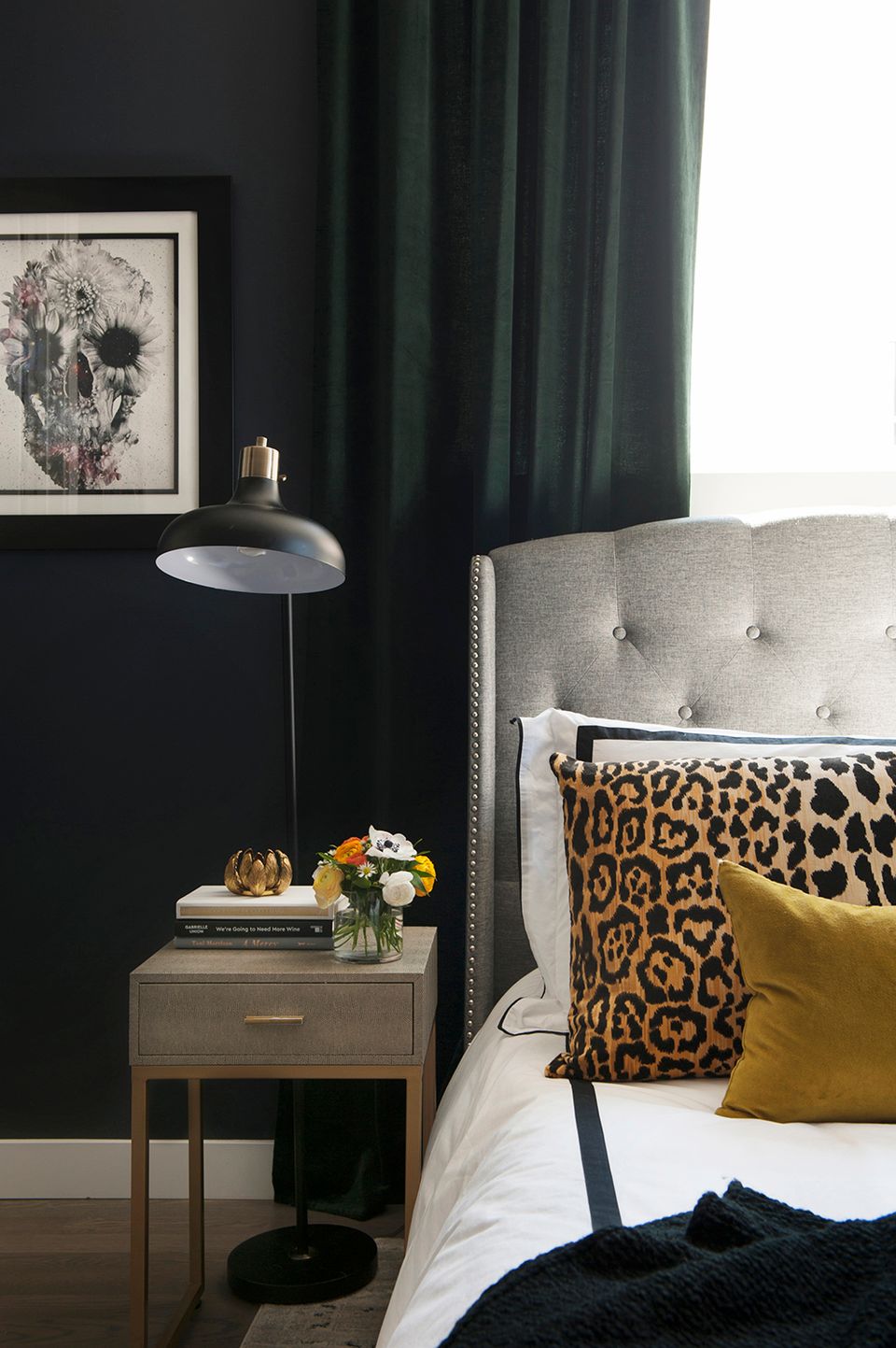 Preppy bedroom with dark forest green walls, cream tufted headboard, leopard print and mustard yellow pillows, and brass accents