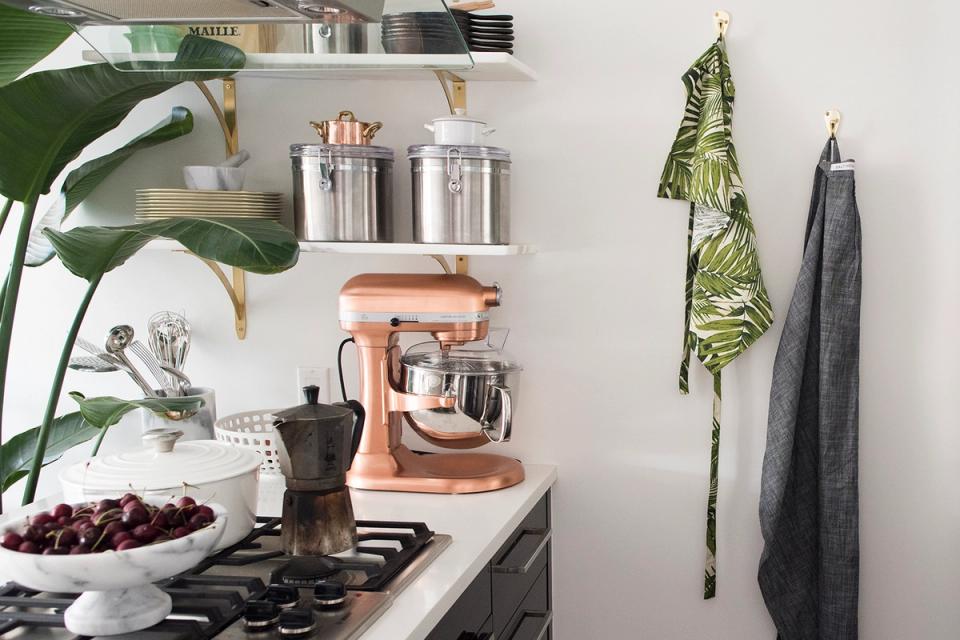 Minimalist kitchen corner with floating shelves, copper appliances, and botanical accents on neutral background