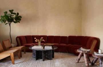 Luxe curved burgundy sectional with warm wood accents and marble-top tables, set against cream walls in a refined, contemporary space