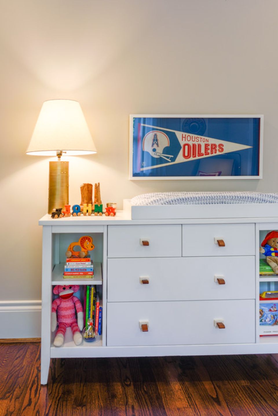 Nursery dresser with warm brass lamp, Houston Oilers pennant, and vintage toy storage styling