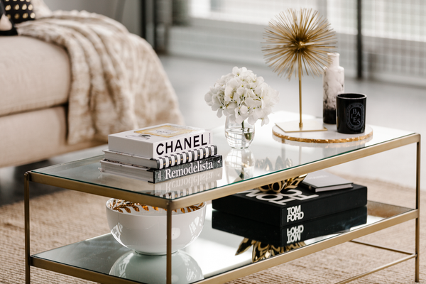 Luxe modern living room with glass and brass coffee table, neutral palette, and curated styling with fashion books and gold accents