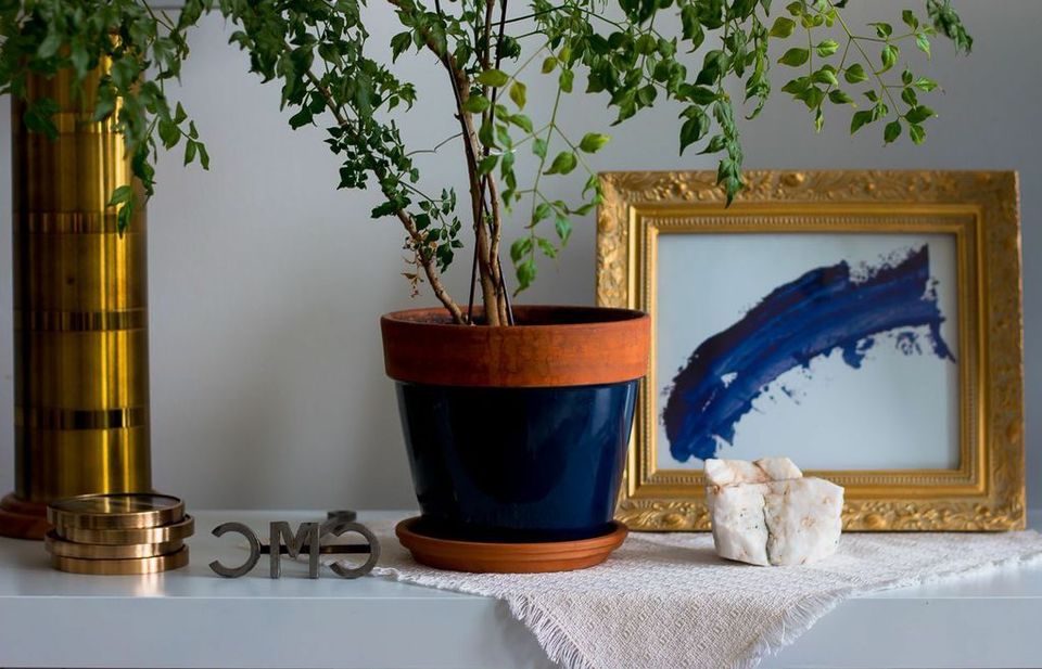 Curated shelf styling with colorblock planter, brass accents, and blue artwork in warm gold frame.
