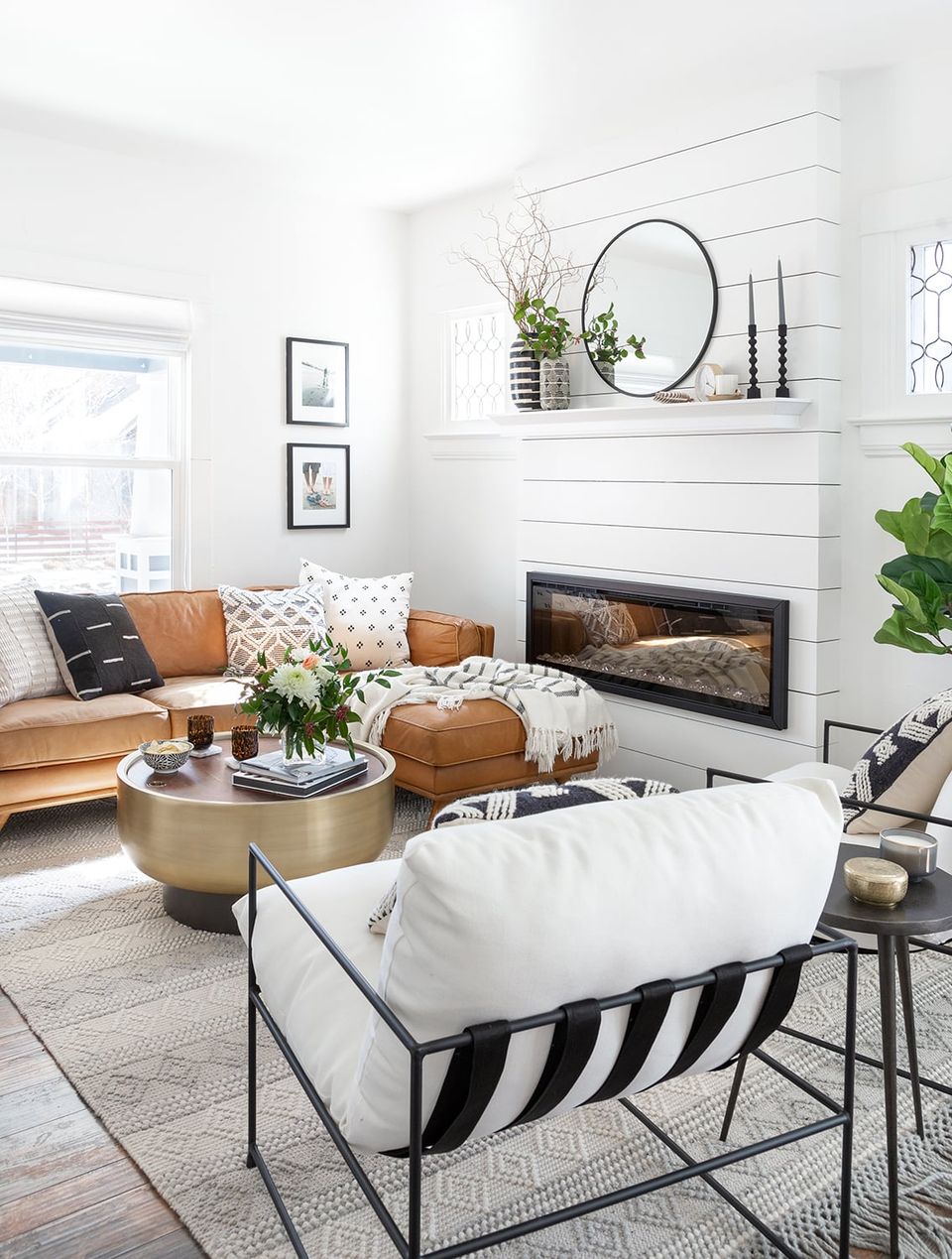 Scandinavian-inspired room with tan leather sofa, linear fireplace, striped accent chair, and brass coffee table in neutral palette.