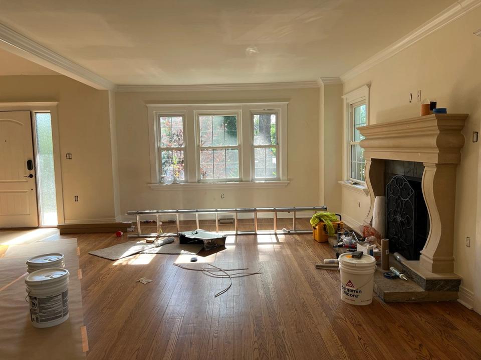 Empty living room during renovation with hardwood floors, fireplace, and natural window light