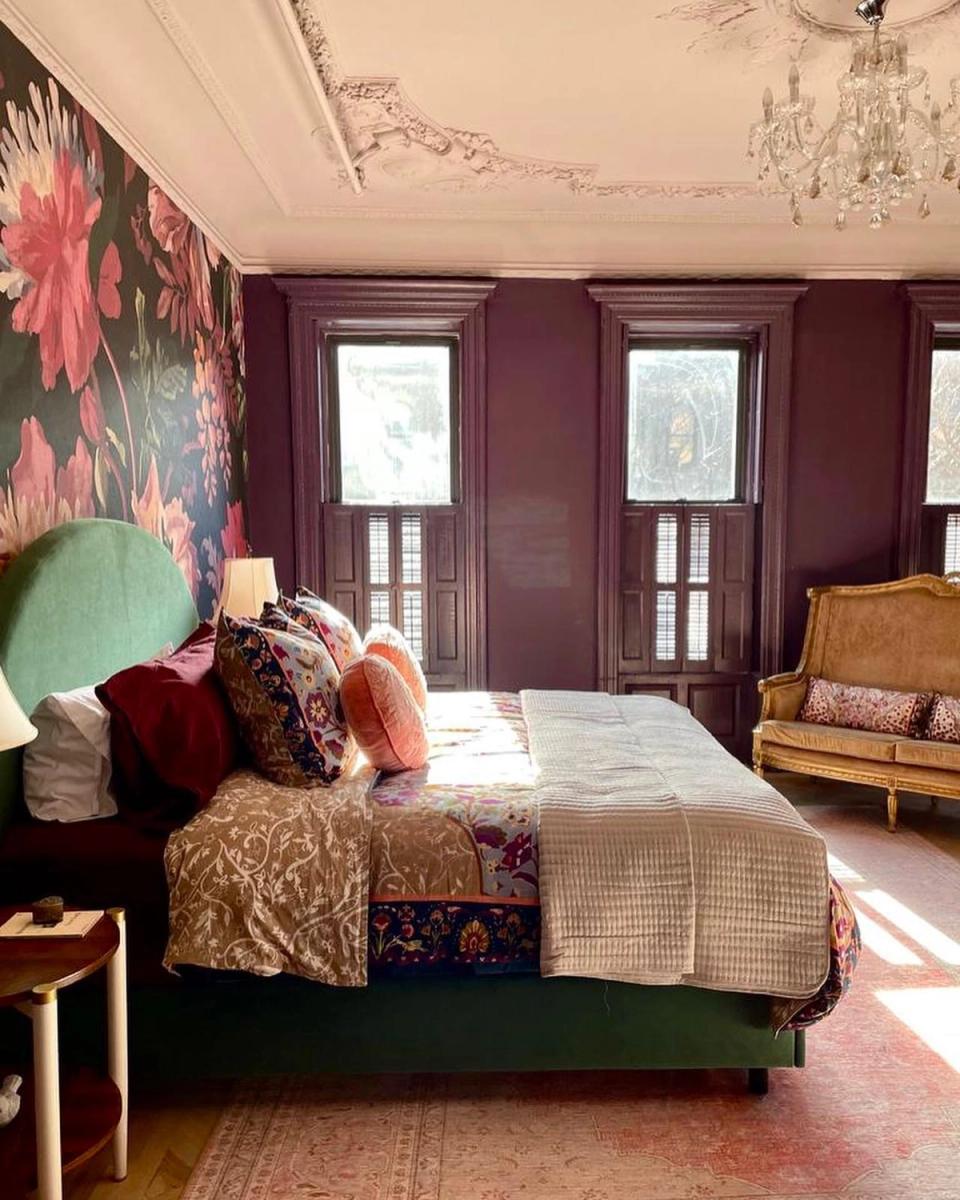 Bold maximalist bedroom in deep plum with floral wall art, layered textiles, and warm vintage touches
