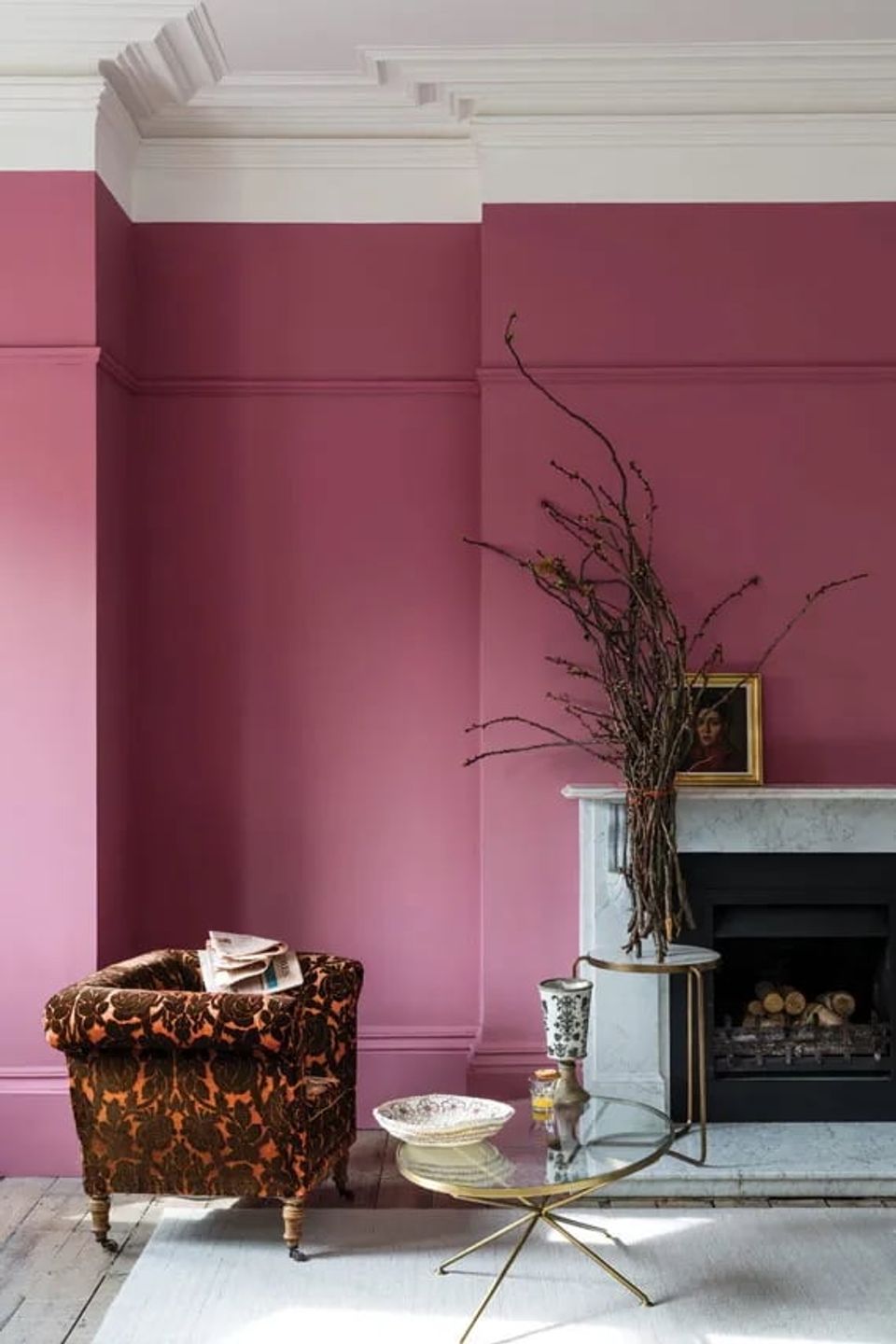 Sophisticated mauve living room with jewel-toned pink accent wall, ornate velvet chair, fireplace, and minimalist botanical styling