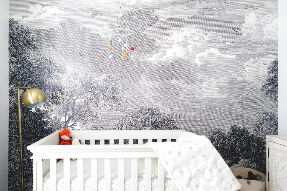 Whimsical nursery with enchanted forest mural, white crib, and warm accent lighting creating a magical atmosphere.