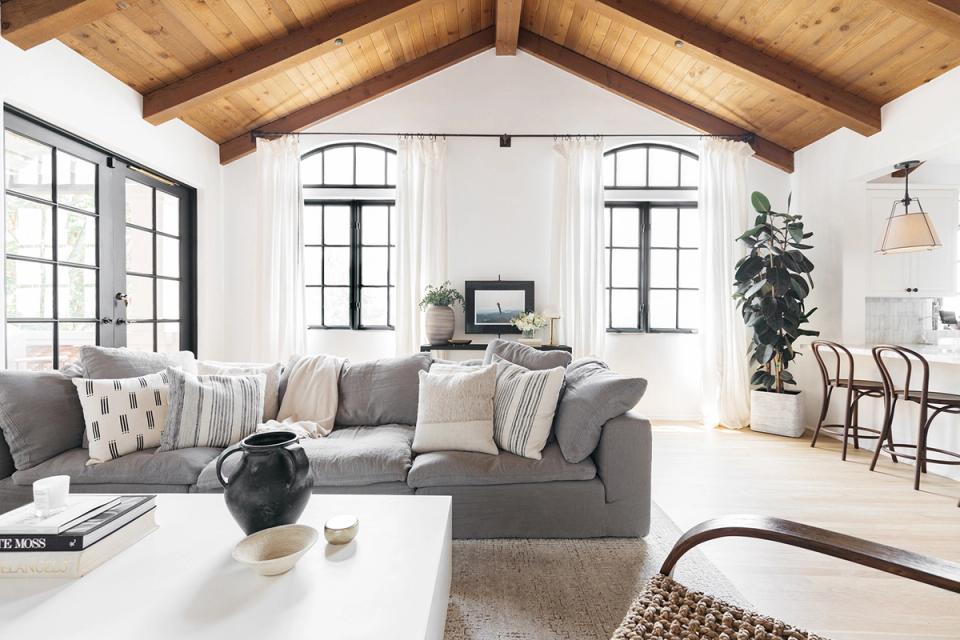 Farmhouse living room with exposed wood beams, neutral sofa, natural light, and minimalist wall styling in soft whites and grays