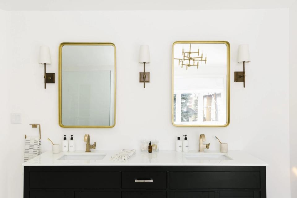 Minimalist bathroom with dual brass-framed mirrors, black vanity, and brass fixtures against white walls