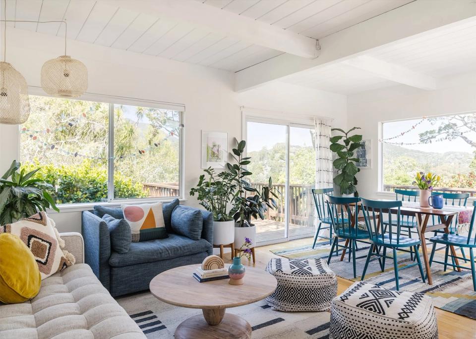 Bright coastal living-dining area with navy blue sofa, natural wood coffee table, and abundant natural light