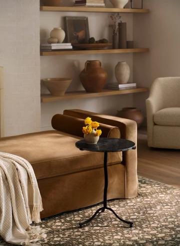 Warm earthy interior with caramel leather ottoman, floating wood shelves, and natural wood accents against neutral backdrop