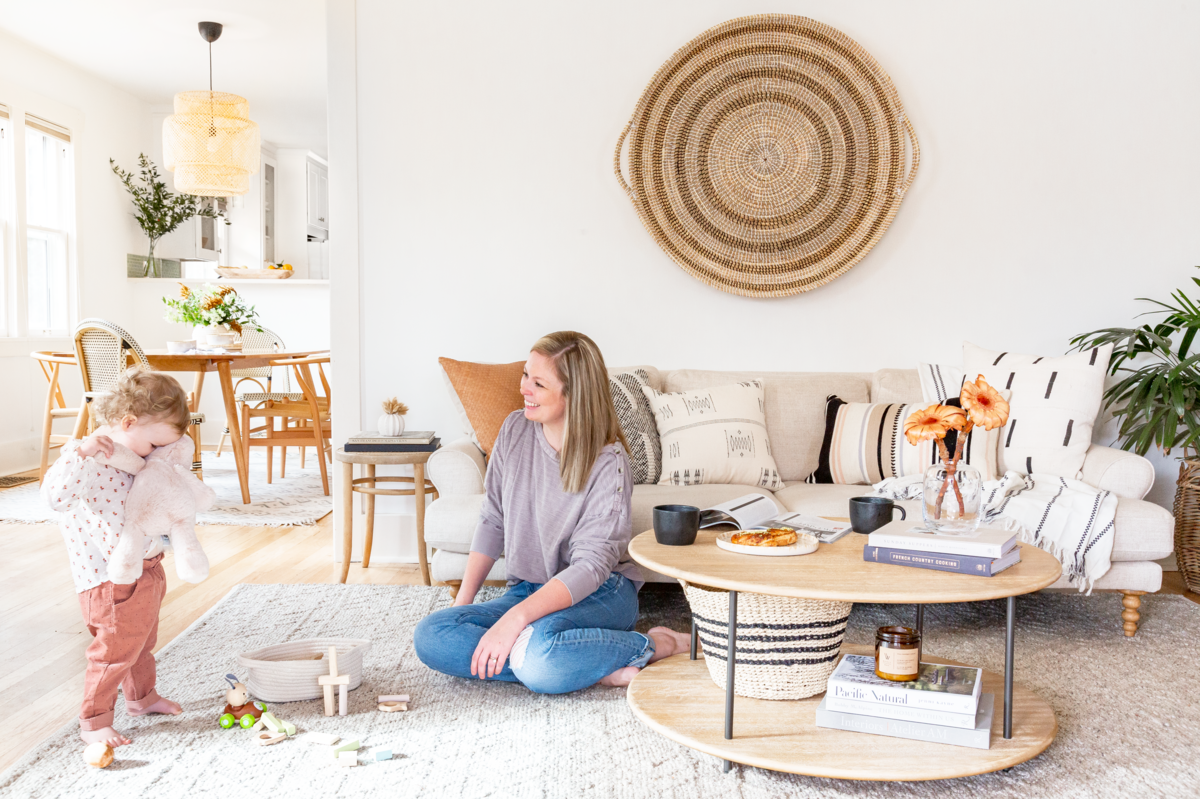 Bright Scandi-boho living room with natural wood furniture, woven wall hanging, and neutral tones, featuring a parent and child playing together