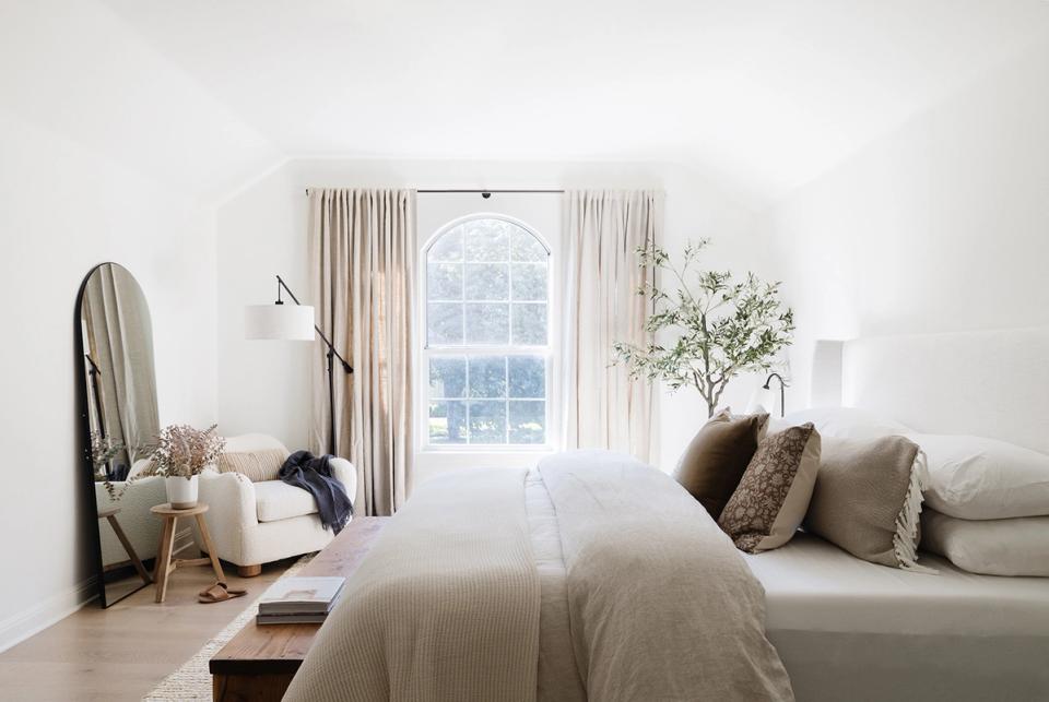 Minimalist primary bedroom with soft neutral palette, linen bedding, and natural light from tall windows embodying calm Texas modern design