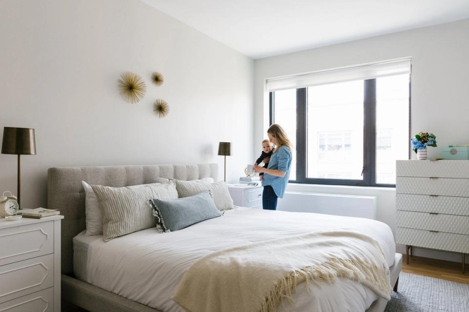 Serene minimalist bedroom with neutral palette, upholstered headboard, layered bedding, and natural light from floor-to-ceiling windows