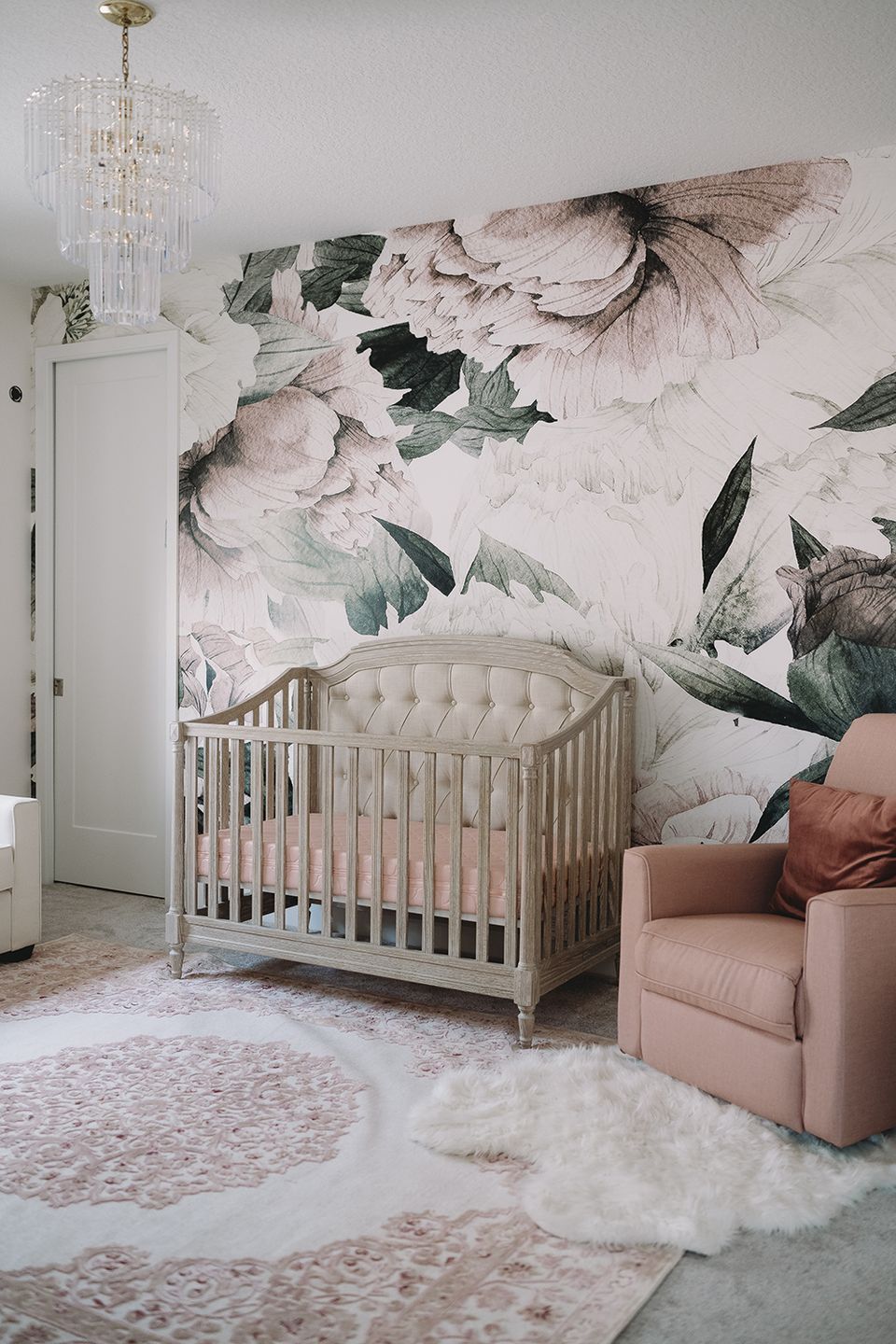 Romantic nursery with oversized floral wallpaper, white crib, blush armchair, crystal fixture