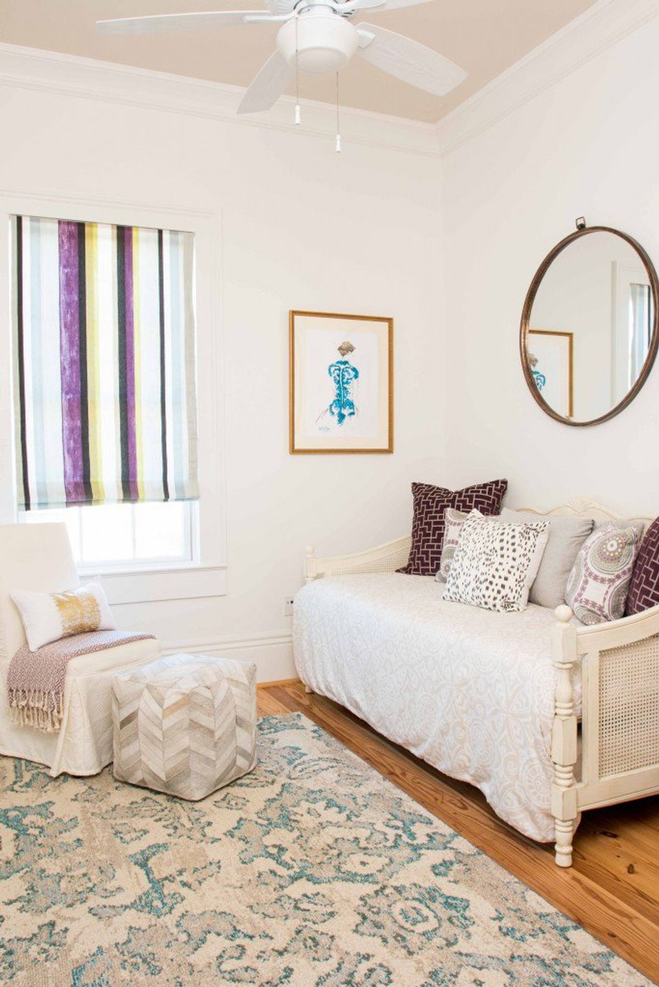 Serene bedroom nook with cream daybed, purple striped curtains, and round wood-framed mirror