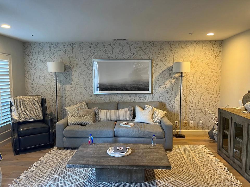 Warm contemporary family room with soft blue sofa, textured wallpaper, and amber lighting creating a cozy, inviting atmosphere.