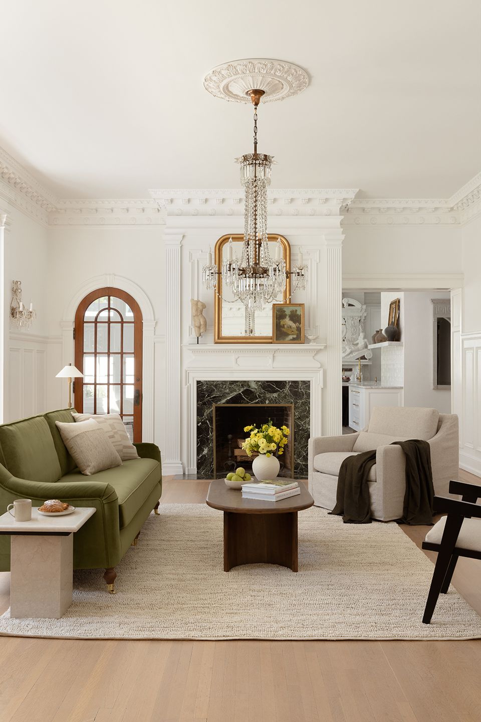 Classic living room with olive accent chair, white fireplace, ornate chandelier, and architectural molding