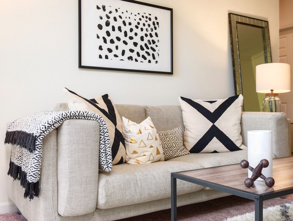 Cozy contemporary sofa with layered pillows, geometric art, warm lighting, and texture-rich styling in neutral tones.