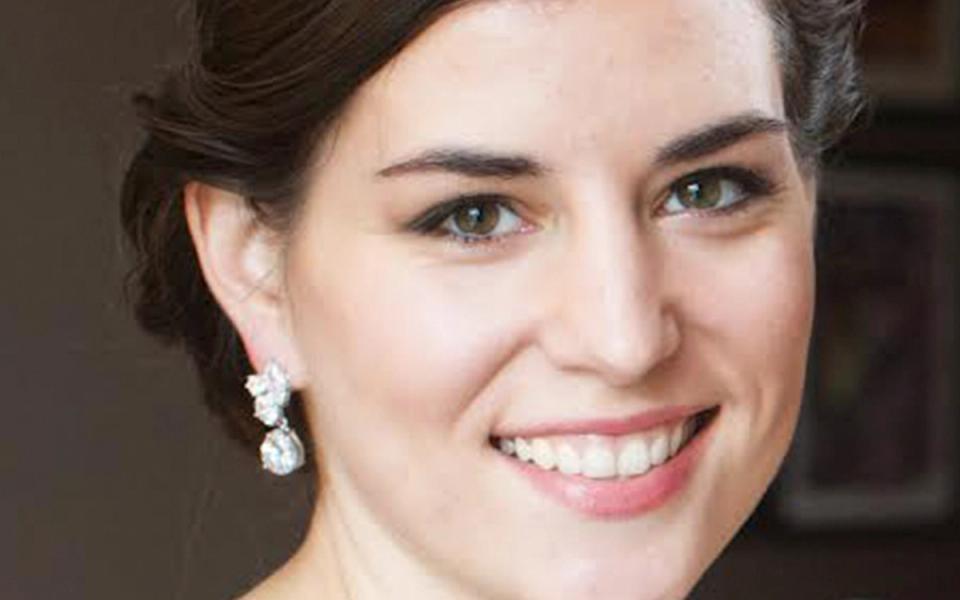 Portrait of a smiling woman with dark hair and pearl earrings against a neutral background
