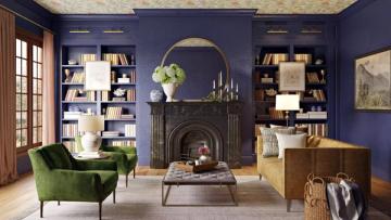 Elegant traditional living room with deep navy walls, arched mirror above fireplace, green velvet chair, and curated shelving creating sophisticated ambiance.