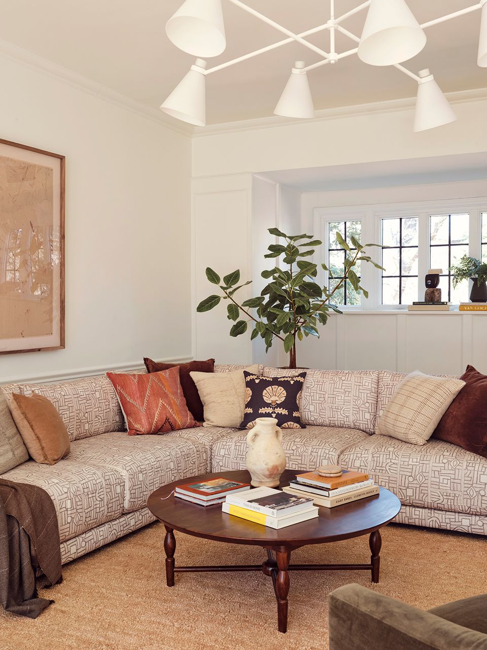 Curved sectional in warm neutrals with rust and navy pillows, complemented by geometric ceiling fixture