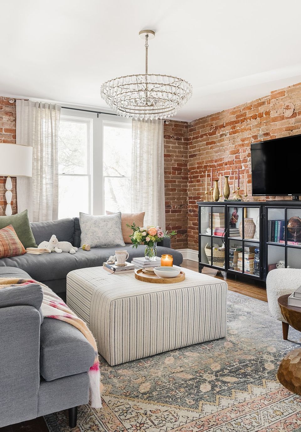 Industrial-eclectic living room featuring warm exposed brick, gray upholstery, and crystal chandelier in contemporary casual setting